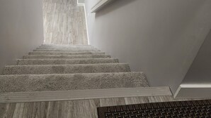 A staircase with a wooden floor leading to a room with a white chair and a light fixture. - Spacious Basement Suite in Bonavista With Separate Entrance (Winnipeg)