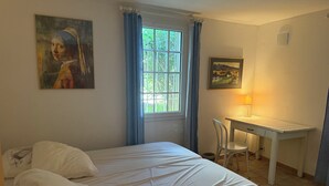 Una camera da letto con un letto, una scrivania, una sedia, una finestra con tende e due quadri appesi al muro.