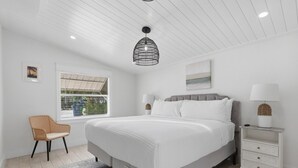 Un dormitorio con cama, una silla, una mesita de noche, una lámpara y una ventana con persianas.