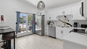 Una cocina moderna con armarios blancos, un refrigerador de acero inoxidable, una encimera negra y una lámpara colgante.