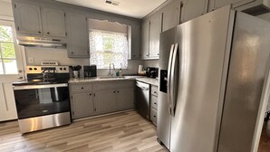 Une cuisine moderne dotée d’appareils électroménagers en acier inoxydable, de planchers en bois clair et d’une fenêtre agrémentée de rideaux à motifs.