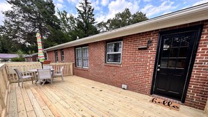 Une terrasse en bois avec une table et des chaises, une porte noire et un bâtiment en briques.