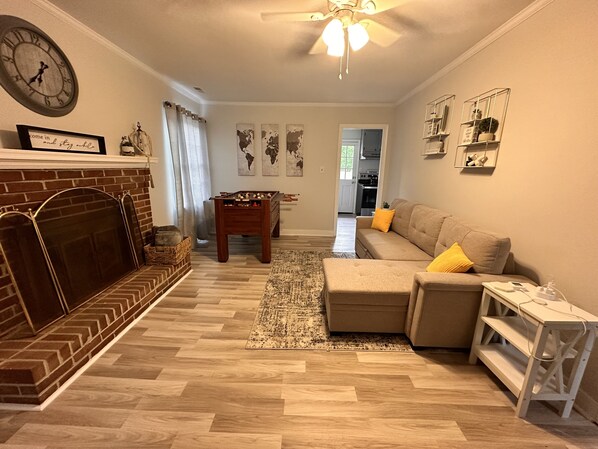 A living room with a fireplace, a sofa, a coffee table, and a foosball table. - Pet Friendly Cozy & Comfy 3 BR House w Large Yard & Deck (Mechanicsville)
