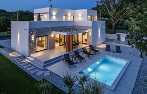 Ein modernes, zweistöckiges Haus mit Swimmingpool, Sitzgelegenheit im Freien und einer Fassade aus Naturstein.