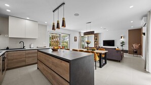 A modern kitchen with a central island, wooden cabinets, and pendant lighting. - Luxurious home in Marasi (Marasi)