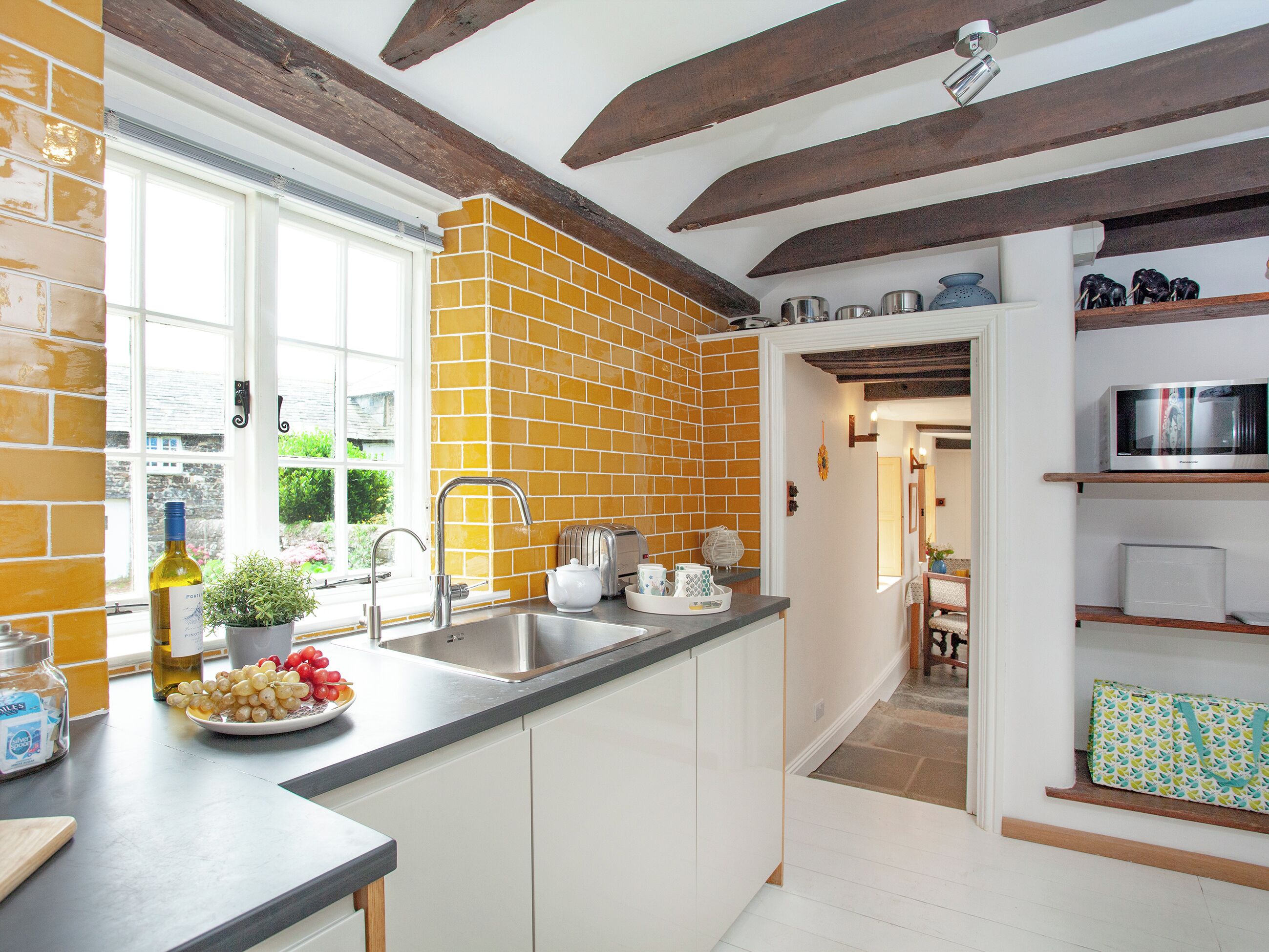 A kitchen with a brick backsplash, white cabinets, and a window.