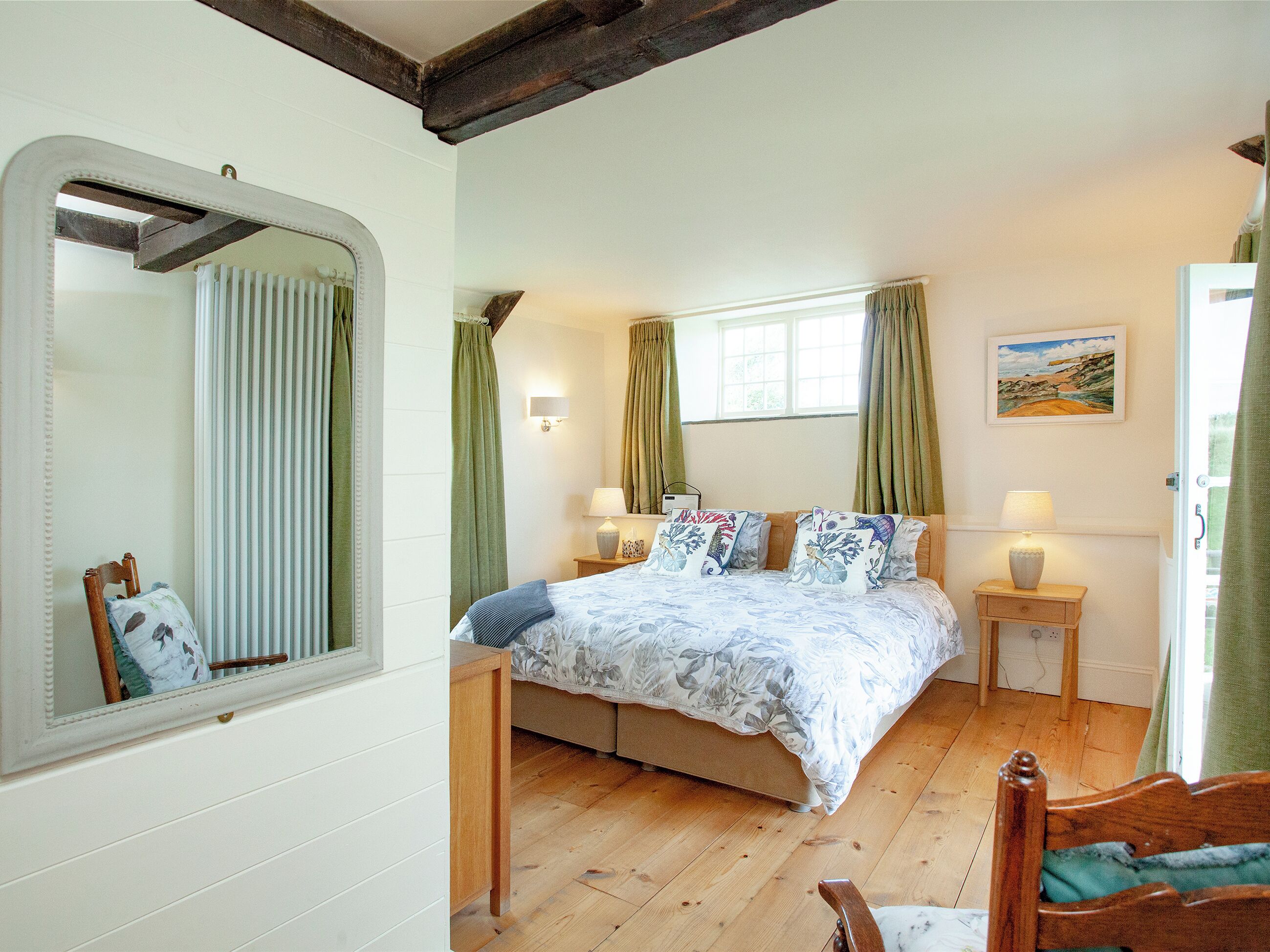 A bedroom with a bed, bedside tables, a mirror, a window with curtains, and a painting on the wall.