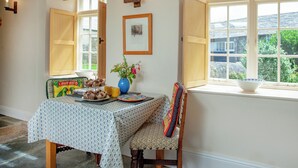 A dining area with a table set for a meal, a vase with flowers, and a window with a view of greenery.