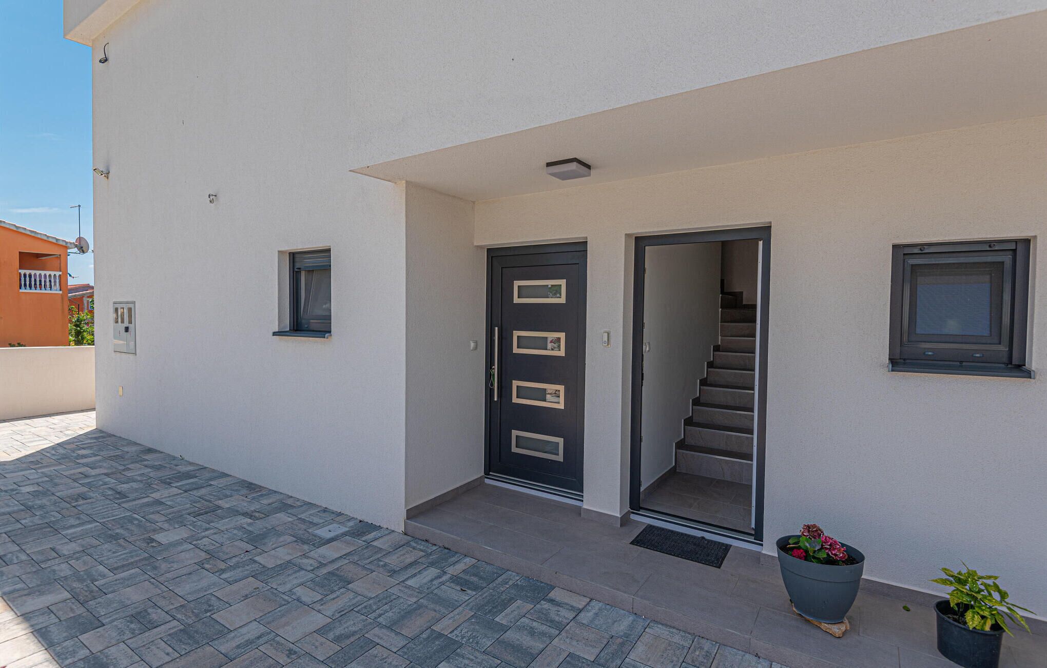A modern building with a white exterior, a dark door with multiple rectangular windows, and a staircase leading to an upper floor.