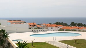 Uma área de piscina com espreguiçadeiras, uma piscina menor e vista para o mar.