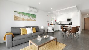 Uma sala de estar moderna com um sofá cinzento, uma mesa de centro e um espaço de jantar com mesa e cadeiras.
