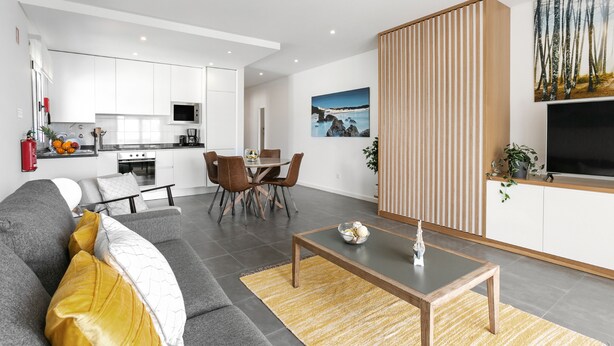 Uma sala de estar moderna com um sofá cinzento, uma mesa de centro de madeira e uma área de refeições com mesa e cadeiras.