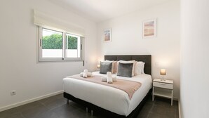 Quarto moderno com uma cama grande, mesa de cabeceira com abajur e janela com vista para o verde.
