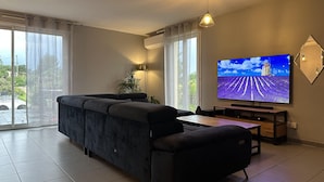 A modern living room with a dark sofa, a flat-screen TV, and a dining table.