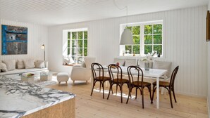 Ett rymligt vardagsrum med ett matbord i marmor, vita soffor och ett stort fönster med utsikt över grönområden.