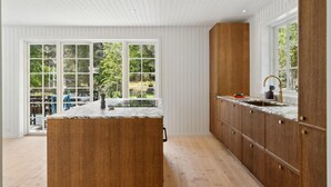 Ett modernt kök med en stor köksö, träskåp och utsikt över en trädgård genom stora fönster.