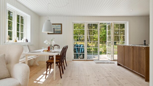 Ett rymligt rum med en matplats, en soffa och ett kök med träskåp.