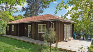 En stuga byggd av trä med en veranda, stora fönster och ett område för grillning.