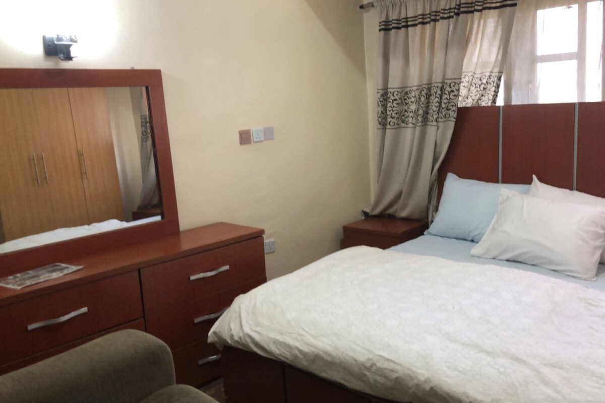 Une chambre à coucher avec une commode en bois, un lit avec une literie blanche et une table de chevet.