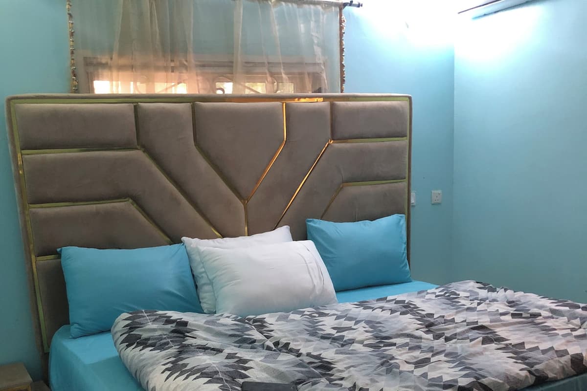 Una cama con colcha de estampado geométrico, cabecera acolchada y almohadas azules y blancas.