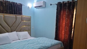 A bedroom with a bed, a chair, a wardrobe, and an air conditioning unit. - Dazzle Hotels and Apartments (Abuja)