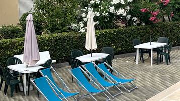 Zona de piscina con sillones, una mesa y sombrillas.