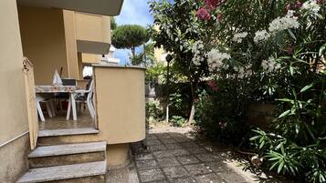 En bostadsbyggnad med en stenlagd innergård, en trappa som leder upp till en balkong samt en mängd olika växter och blommor.