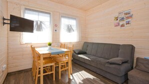 Ein gemütliches Zimmer mit Holzvertäfelung, einem grauen Sofa, einem Holzesstisch mit Stühlen und einem an der Wand montierten Fernseher.