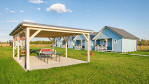 Ein Campingplatz mit überdachtem Picknickbereich, Gartenmöbeln und einer Reihe von blauen Holzhütten.