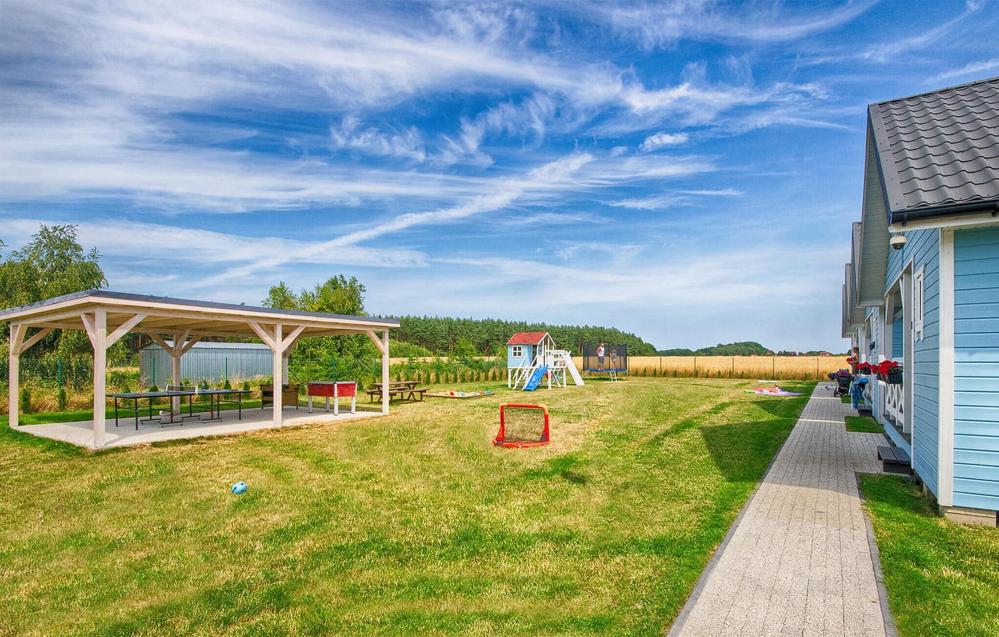 Un'area picnic coperta con panche, una piccola casetta gioco e un parco giochi con uno scivolo.