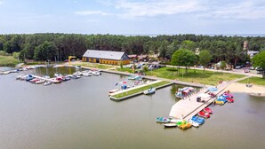 Eine Marina mit mehreren Anlegestellen und Booten, ein großes Gebäude mit geneigtem Dach und ein bewaldeter Bereich im Hintergrund.