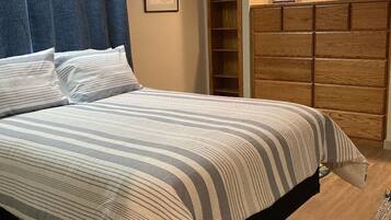 Une chambre à coucher avec un lit, une armoire en bois, un tableau encadré au mur et un rideau bleu.