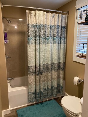 A bathroom with a shower curtain, a toilet, and a window with blinds. - Updated family home in quiet neighborhood. (El Dorado)