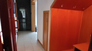 Un couloir avec une porte en bois, un petit banc en bois et un sol carrelé.