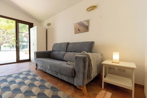 Ein modernes Wohnzimmer mit einem grauen Sofa, einem gemusterten Teppich, einem kleinen Tisch mit einer Lampe und einem Bild an der Wand.