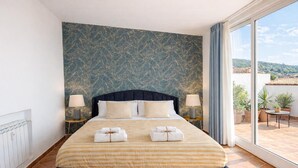 A hotel room with a large bed, two bedside tables, a window with curtains, and a view of the outside.
