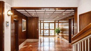 A hotel lobby with wooden paneling, a marble floor, a staircase, and a potted plant.
