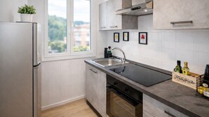 A modern kitchen with a built-in oven, a stainless steel sink, and a window with a view of greenery.