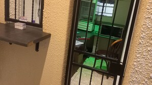 Une pièce avec une fenêtre grillagée, une petite étagère et un objet vert à l’extérieur.