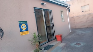 Un bâtiment sur lequel on peut voir un panneau indiquant qu’il est sous surveillance, une porte grillagée et une petite plante en pot.