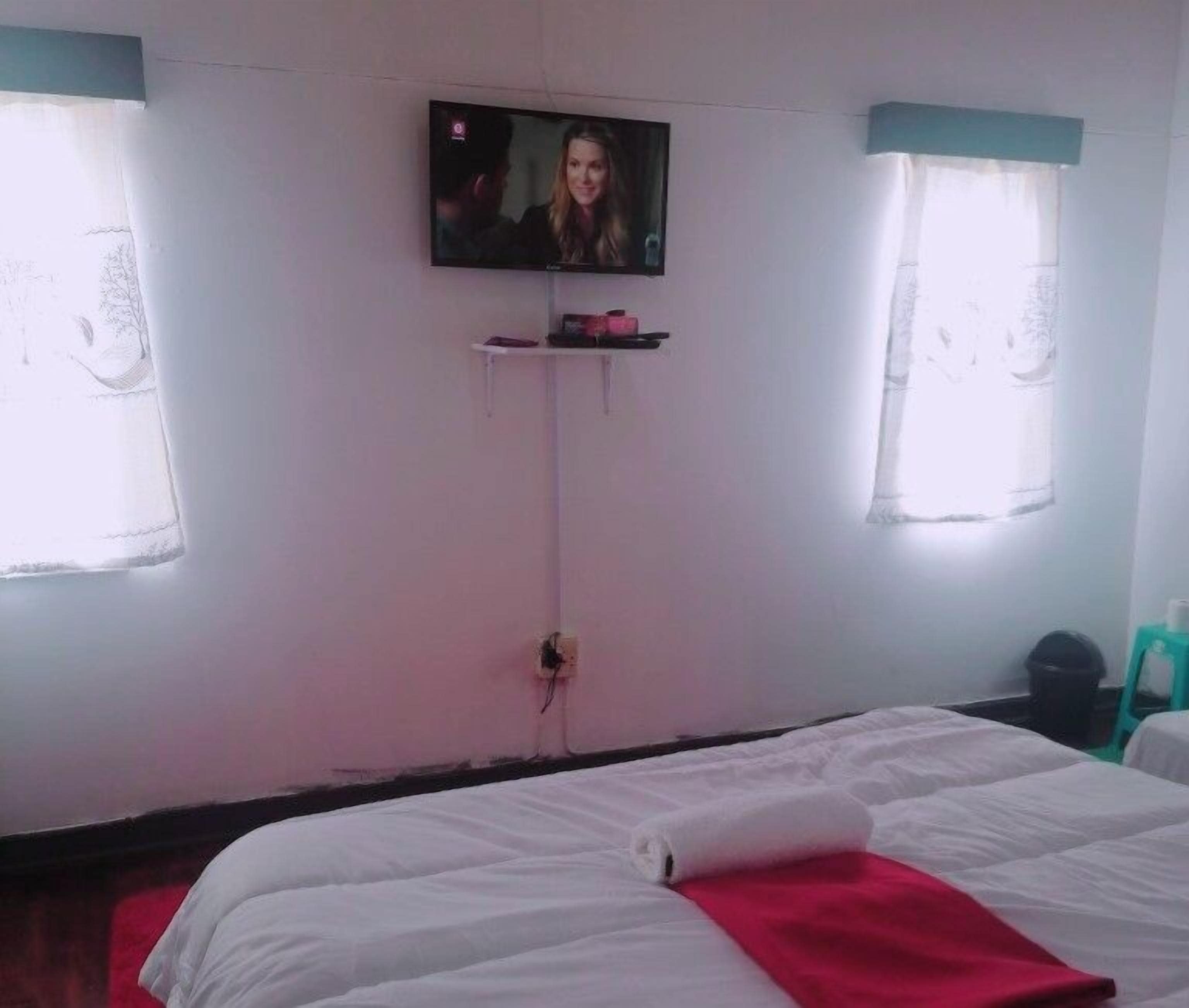 Quarto de hotel com cama, televisão presa na parede e janela com cortinas.