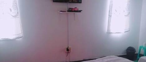 Quarto de hotel com cama, televisão presa na parede e janela com cortinas.