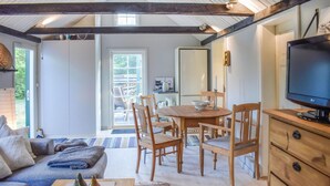 A cozy living room with a sofa, wooden dining table, and chairs. A television is on a wooden cabinet. - Pet friendly home in Beddingestrand (Beddingestrand)