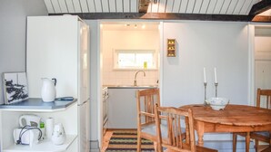 A compact kitchen with a wooden dining table and chairs, a white refrigerator, and a small window above the sink. - Pet friendly home in Beddingestrand (Beddingestrand)