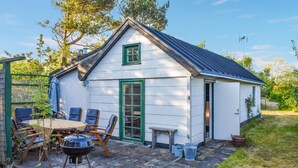 A small white building with a green door and window, a patio with chairs and a table, and a barbecue grill. - Pet friendly home in Beddingestrand (Beddingestrand)