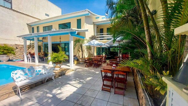 A poolside area with outdoor seating, a covered patio, and lush tropical plants. - POUSADA OCEANIC (Arraial do Cabo)
