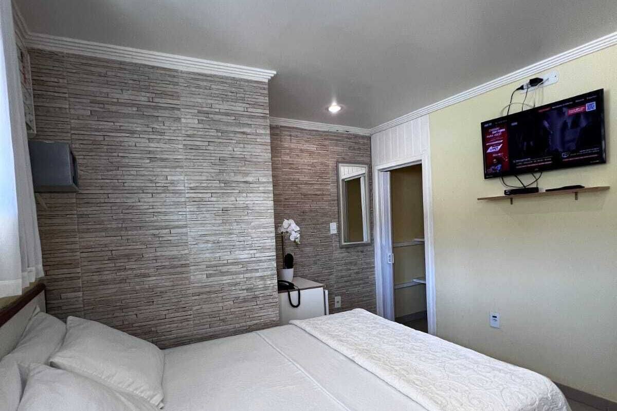 A bedroom with a bed, a television mounted on the wall, and a stone-patterned wall.