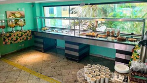 A buffet area with a glass display case, a counter with food items, and a table with stacked cups. - POUSADA OCEANIC (Arraial do Cabo)
