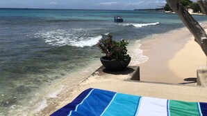 A beach with clear turquoise water, a boat in the distance, and a lounge area with a striped towel. - Beachfront 2 bedroom apartment with private pool -NEW LISTING (Fitts Village)