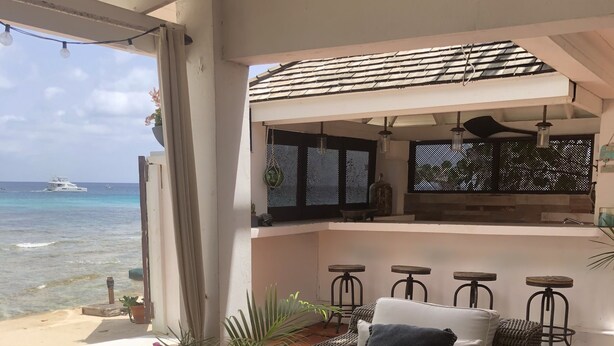 A cozy outdoor seating area with wicker furniture, a glass-top table, and a view of the ocean. - Beachfront 2 bedroom apartment with private pool -NEW LISTING (Fitts Village)